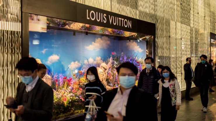 Pejalan kaki yang mengenakan topeng pelindung berjalan melewati LVMH Moet Hennessy Louis Vuitton SE di distrik Tengah Hong Kong, Cina, pada hari Selasa, 11 Februari 2020. Paul Yeung | Bloomberg | Getty Imagesicture